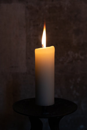 One large burning candle on a metal stand against a stone wall background