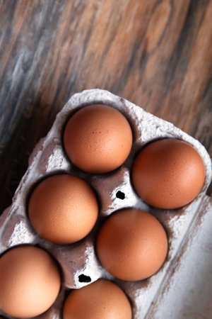 Six brown organic eggs in a cardboard tray on a wooden background. Top view, copy space