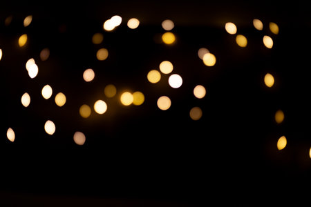 Bokeh golden bright glow lights. Blurred lights of Christmas festive garland on a black backgroundの写真素材