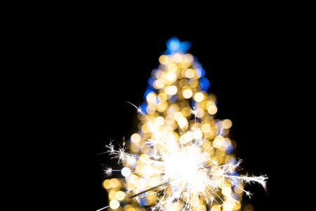 A beautifully blurred Christmas tree with sparkler decorated with warm golden and cool blue lights,...