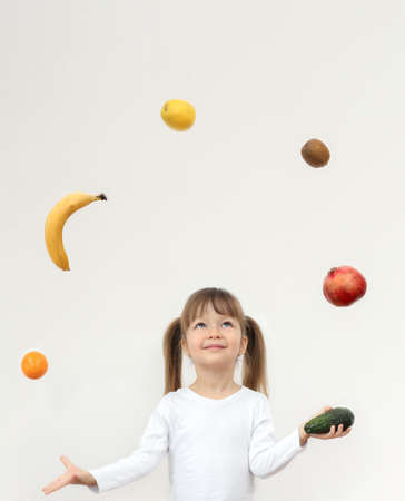 A little funny girl juggles fruit on grey backgroundの写真素材