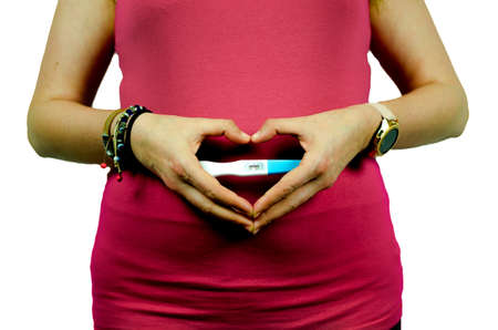 close up woman holding pregnant test positive in hands with heart shapeの写真素材