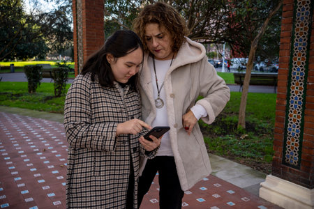 Hispanic teenage girl and her affectionate mother looking at a smartphone and smilingの写真素材