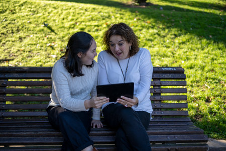 mother and daughter looking at each other sitting on a park bench. single parent family conceptの写真素材