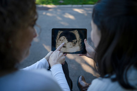 mother showing her asian daughter an ultrasound scan of a new baby on a digital tablet.の写真素材