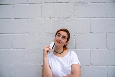 Smiling young woman standing near wall with credit cardの写真素材
