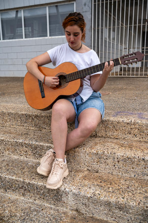 Happy young ethnic woman standing and playing guitar