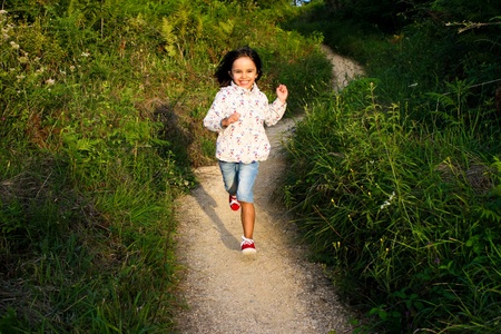 Happy little girl running down a winding path in the countryside at sunsetの写真素材