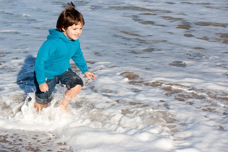 Happy child wetting the clothes while escaping the waves in winterの写真素材