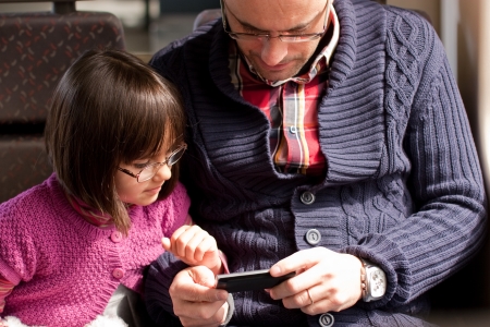 Father and daughter with glasses watching a video on the moile phone while traveling in trainの写真素材