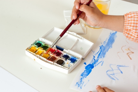 Hand of child with paintbrush taking paint on watercolor setの写真素材
