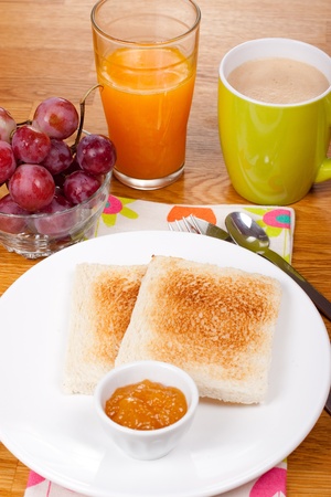 Breakfast with toast, jam, orange juice, coffee with milk and grapesの写真素材
