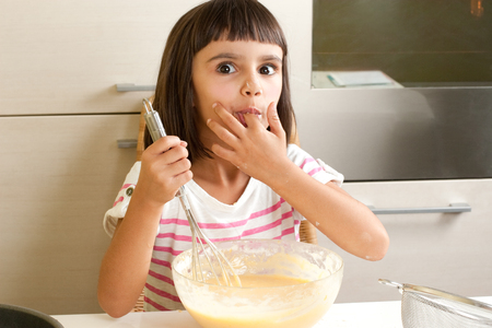 Happy and funny little girl sucking the mixture to cook a cakeの写真素材