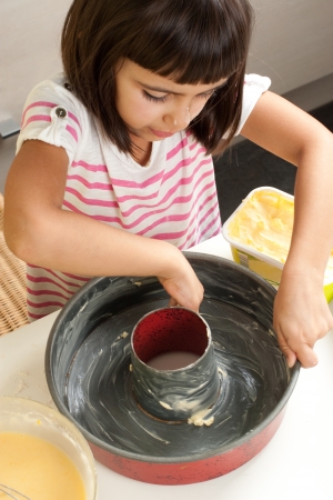 Happy little girl greasing a mold with hand to bake a cakeの写真素材