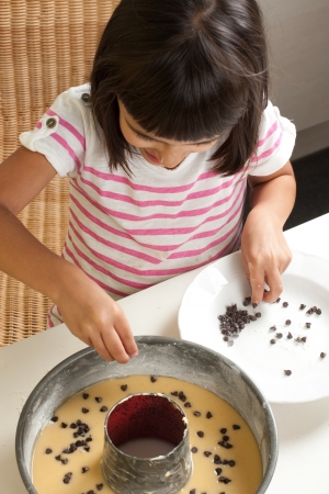 Happy little girl pouring chocolate chips to cakeの写真素材