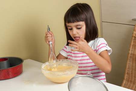 Happy little girl sucking the mixture to cook a cakeの写真素材