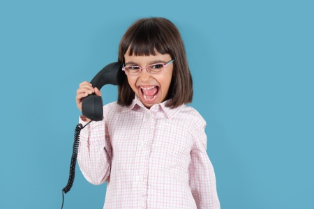 Funny little girl with glasses screaming at retro phoneの写真素材