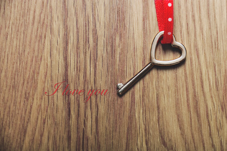Heart shaped key tied with a red and dots ribbon on wood . Valentines card.