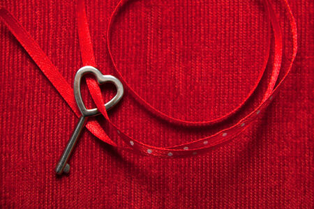 Heart shaped key tied with a red and dots ribbon on red velvet . Copy space.の写真素材