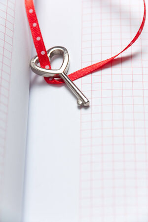 Heart shaped key tied with a red and dots ribbon on notebook . Copy spaceの写真素材