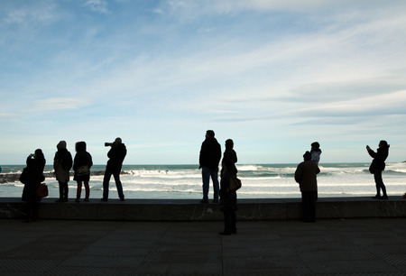 Silhouettes of people watching, photographing and recording with mobiles waves during stormy weather in winterのeditorial素材