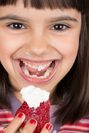 Close up of cute and happy little girl eating a big strawberry with creamの写真素材