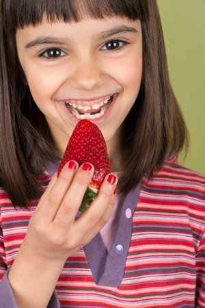 Cute and happy little girl  with red nail polish eating a big strawberryの写真素材