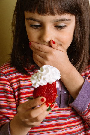 Surprised and happy young girl holding a big strawberry with cream  Film grain effect added の写真素材