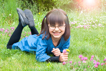 Cute and happy little girl with glasses picking wild flowers lying in the grassの写真素材