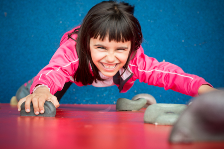 Pretty girl climbing a red wall in a playgroundの写真素材