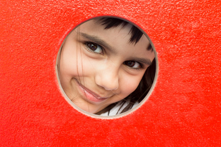 Pretty little girl peeking through a hole in a playgroundの写真素材