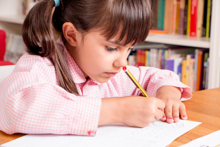 Cute little girl in uniform doing calligraphy exercises の写真素材