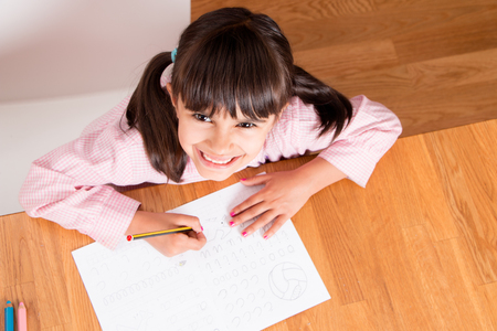 Happy little girl in uniform doing calligraphy exercises  Top viewの写真素材