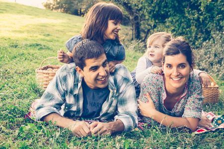 Happy family of four lying in the grass in autumn after picking apples. Warm effect added.の写真素材