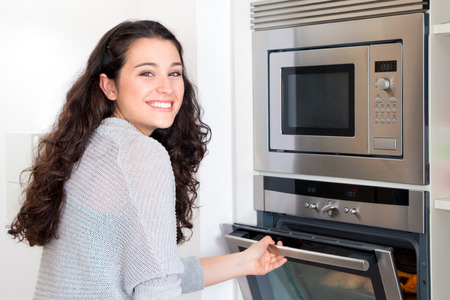 Happy young beautiful woman opening the oven door to control the roastの写真素材