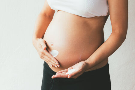 Belly of a pregnant woman applying moisturizer