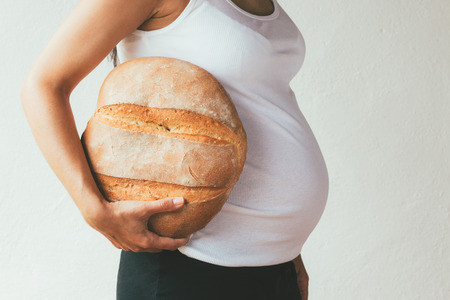 Unrecognizable pregnant woman with a loaf of bread under her arm Concept of fortune  when having a babyの写真素材
