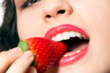 Close up of sexy woman mouth with red lips biting strawberryの写真素材