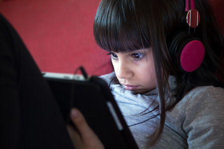 Portrait of a cute little girl with headphones using a tablet pc at homeの写真素材