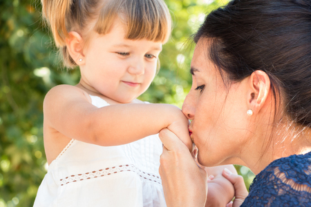 Mother kissing little daughter hand outdoors. Focus on mumの写真素材