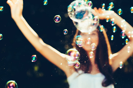Girl with arms raised dancing with bubbles outdoors. Girl is defocusedの写真素材
