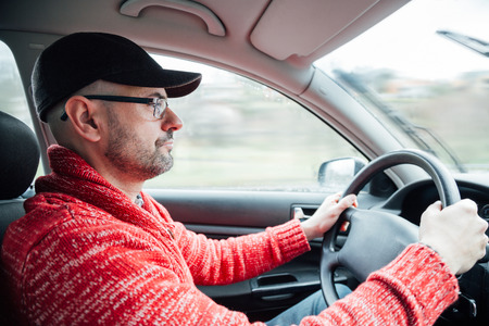 Concentrated man with cap and glasses driving his car in a rainy dayの写真素材
