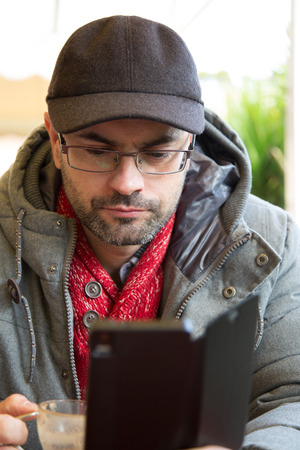 Man with cap using his smartphone while having a coffe in a terrace in winterの写真素材