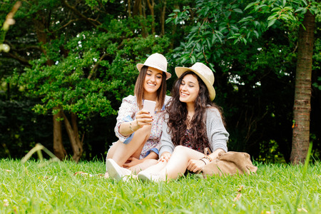 Cute girl friends sitting on the grass making a selfie with a mobileの写真素材