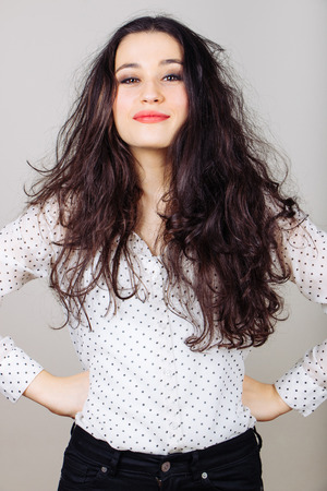 Beautiful and funny brunette girl in polka dots shirt with tousled hair and hands on hipsの写真素材