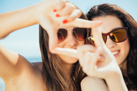 Girl friends on the beach framing with hands as if they were taking picturesの写真素材