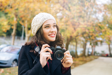 Happy young beautiful woman with an analog camera capturing autumn in the cityの写真素材