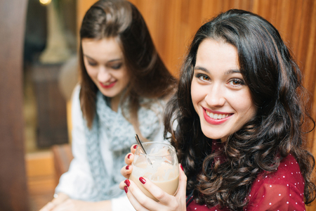 Beautiful young woman having a coffee with a friend looking at camera
