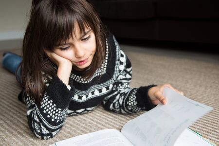 Cute little girl lying on the carpet reading a book