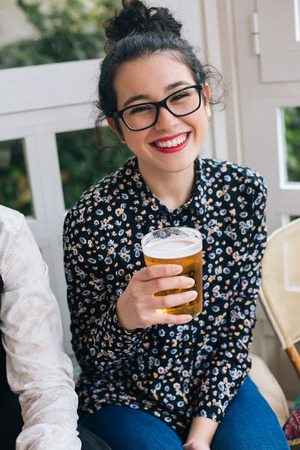 Portrait of a young cute modern woman drinking beer in a bar with friendsの写真素材